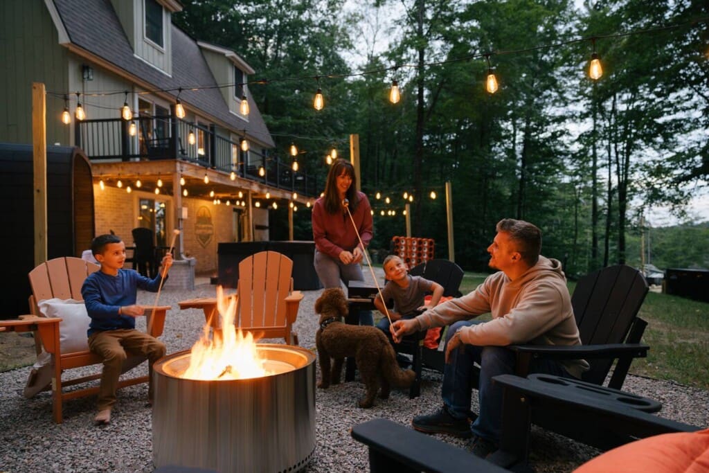 Family roasting marshmallows at fire pit with Adirondack chairs and string lights at Peak and Pine Retreat