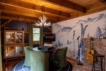 Cozy cocktail lounge with antler chandelier, mountain mural, and karaoke corner at Peak and Pine Retreat
