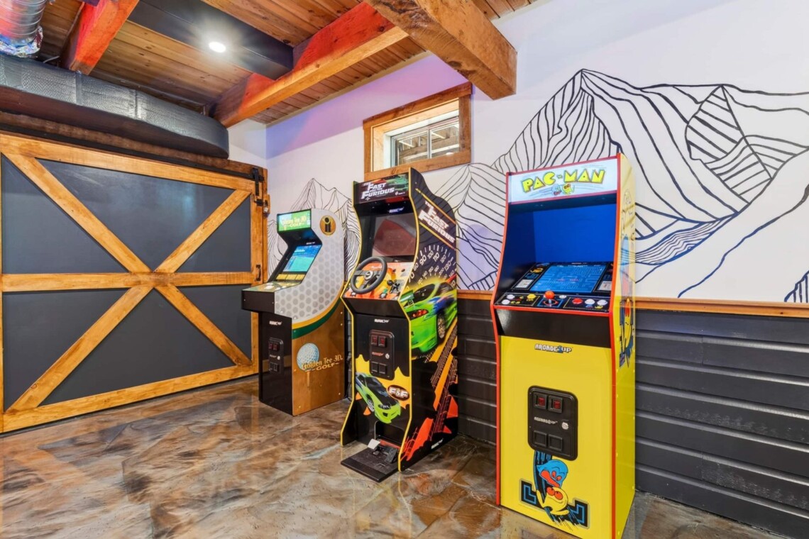 Game room with Pac-Man and racing arcade machines beside a mountain line-art mural