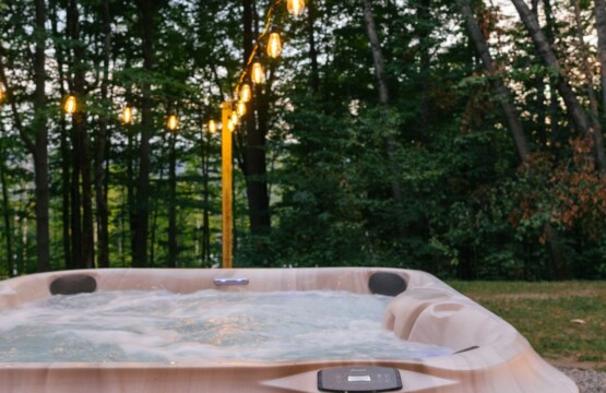 Outdoor hot tub glowing at dusk under string lights in the wooded backyard