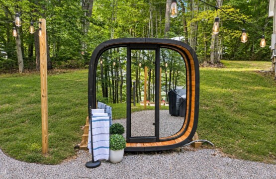 Outdoor glass-front sauna on a gravel pad surrounded by trees at Peak & Pine Retreat