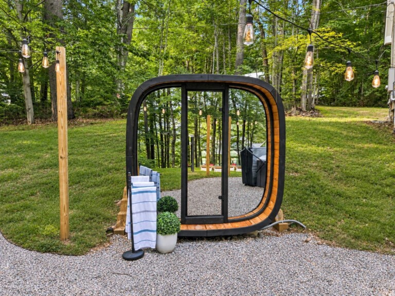 Outdoor glass-front sauna on a gravel pad surrounded by trees at Peak & Pine Retreat