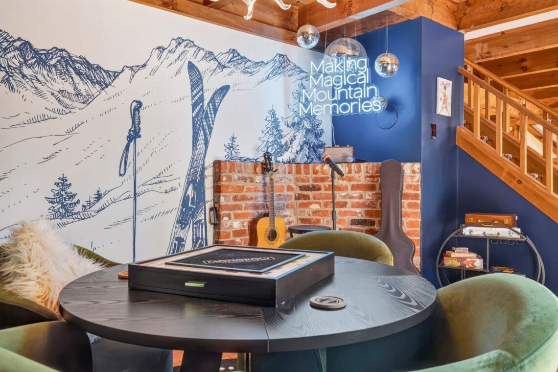 Round game table with green velvet chairs, ski mural and neon sign