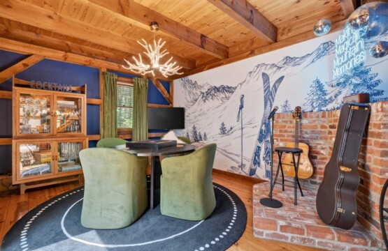 Lounge with acoustic guitars, brick accent wall and green velvet game table chairs