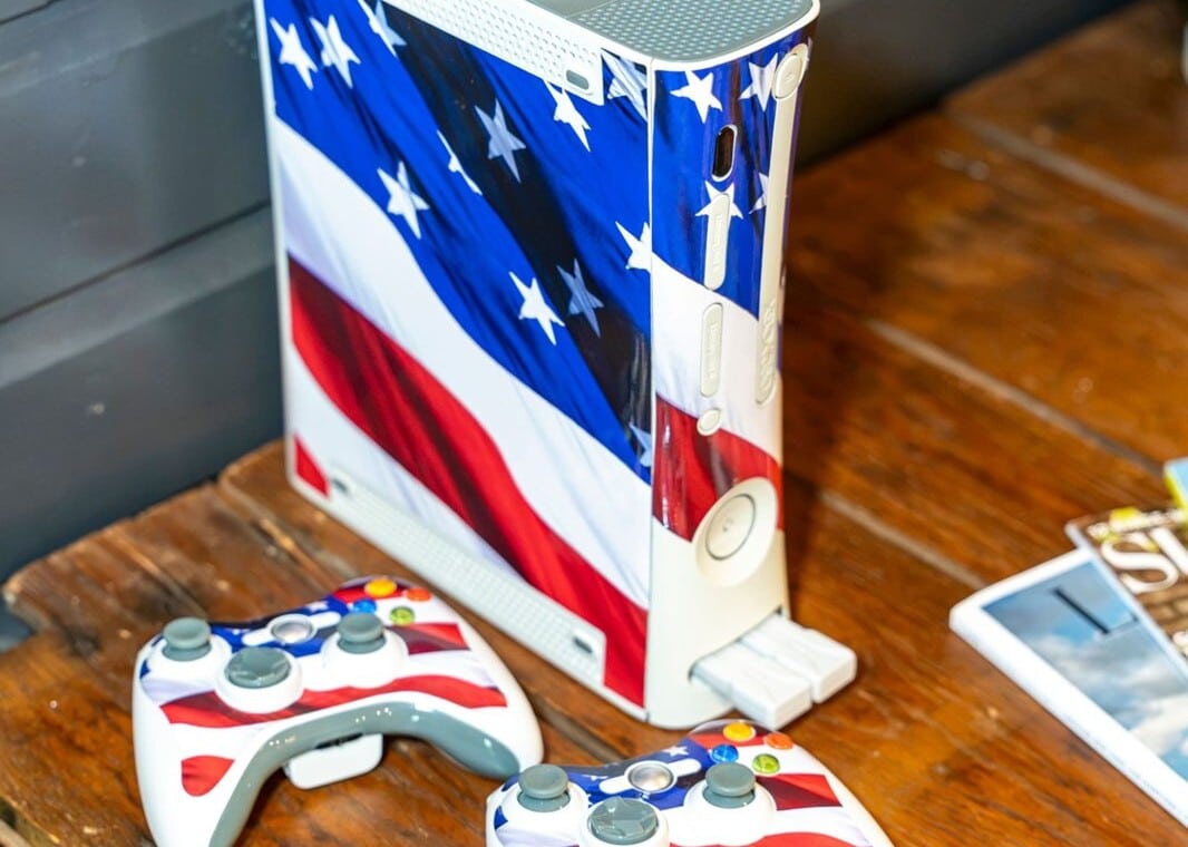 Xbox console with American flag design and matching controllers on a wood table