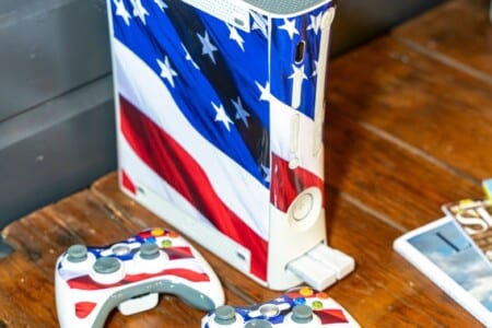 Xbox console with American flag design and matching controllers on a wood table