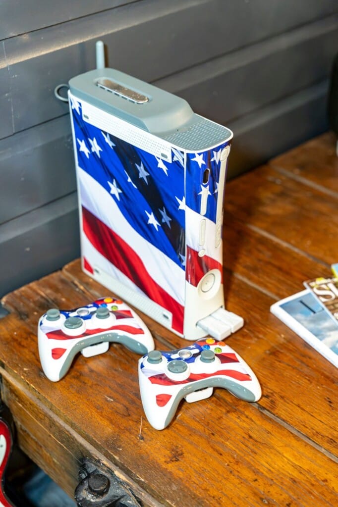 Xbox console with American flag design and matching controllers on a wood table
