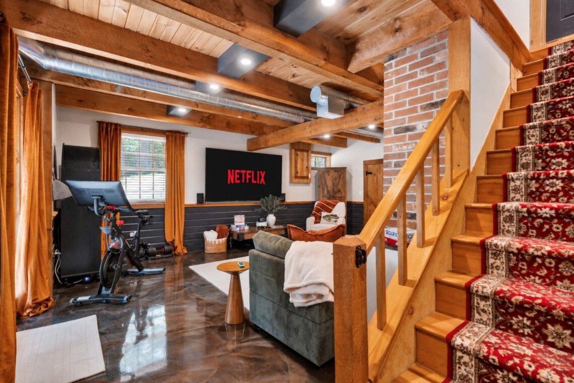 Lower-level lounge with Peloton bike, sectional sofa and carpeted wooden staircase