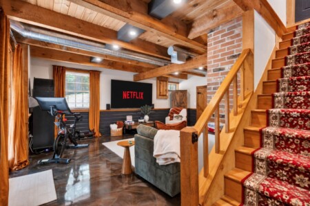 Lower-level lounge with Peloton bike, sectional sofa and carpeted wooden staircase