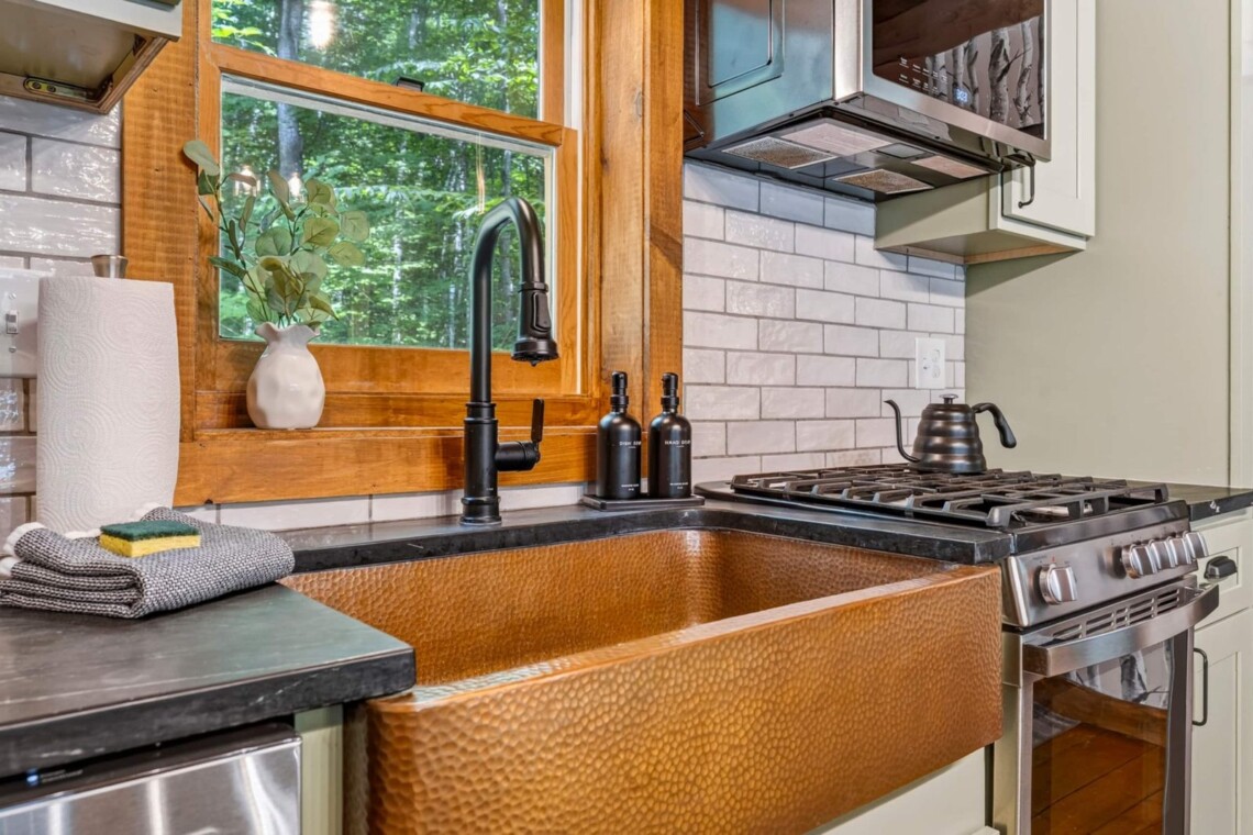 Hammered copper farmhouse sink beside a stainless gas range in the renovated kitchen