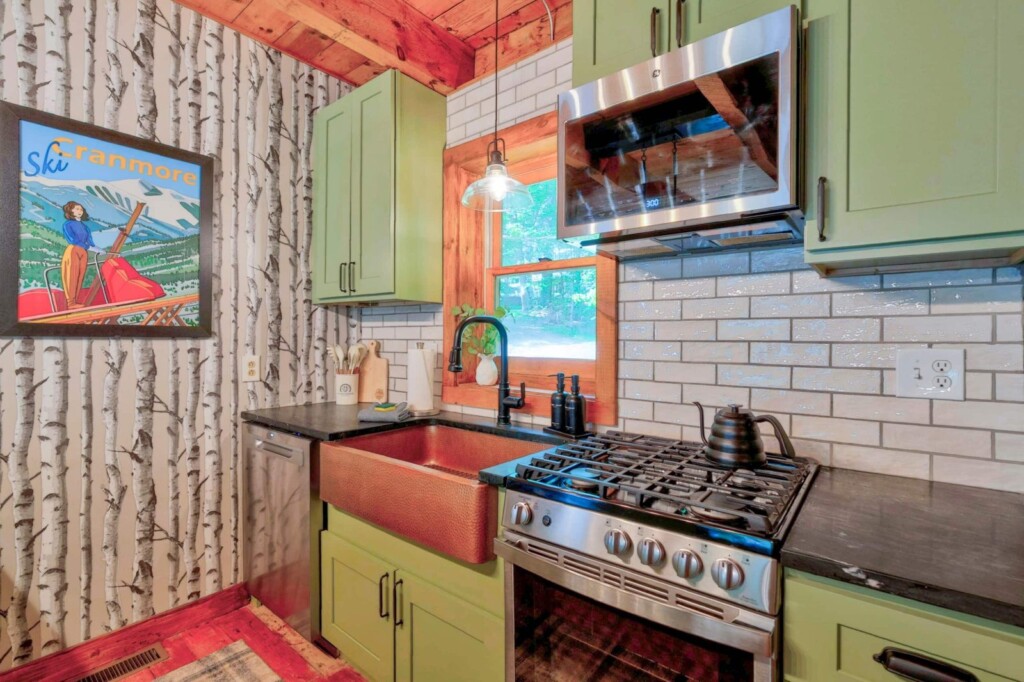 Stainless gas range, copper sink and sage green cabinets with subway tile