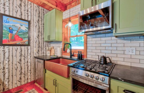 Stainless gas range, copper sink and sage green cabinets with subway tile
