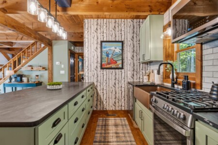 Galley-style kitchen with green cabinets, birch wallpaper and view toward the stairs