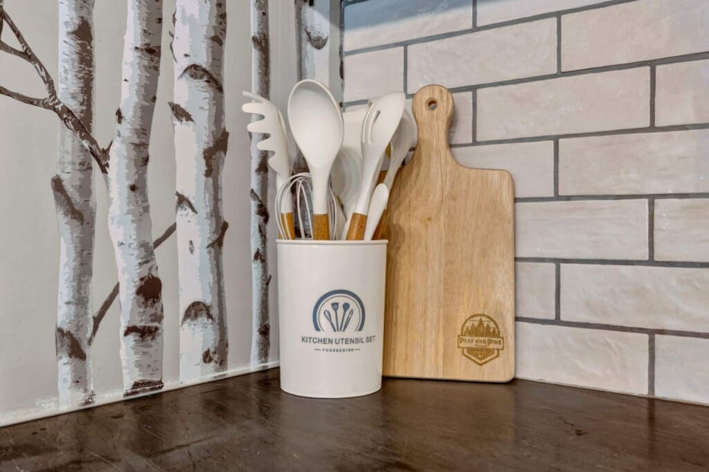 Utensil crock and wooden cutting board against birch tree wallpaper