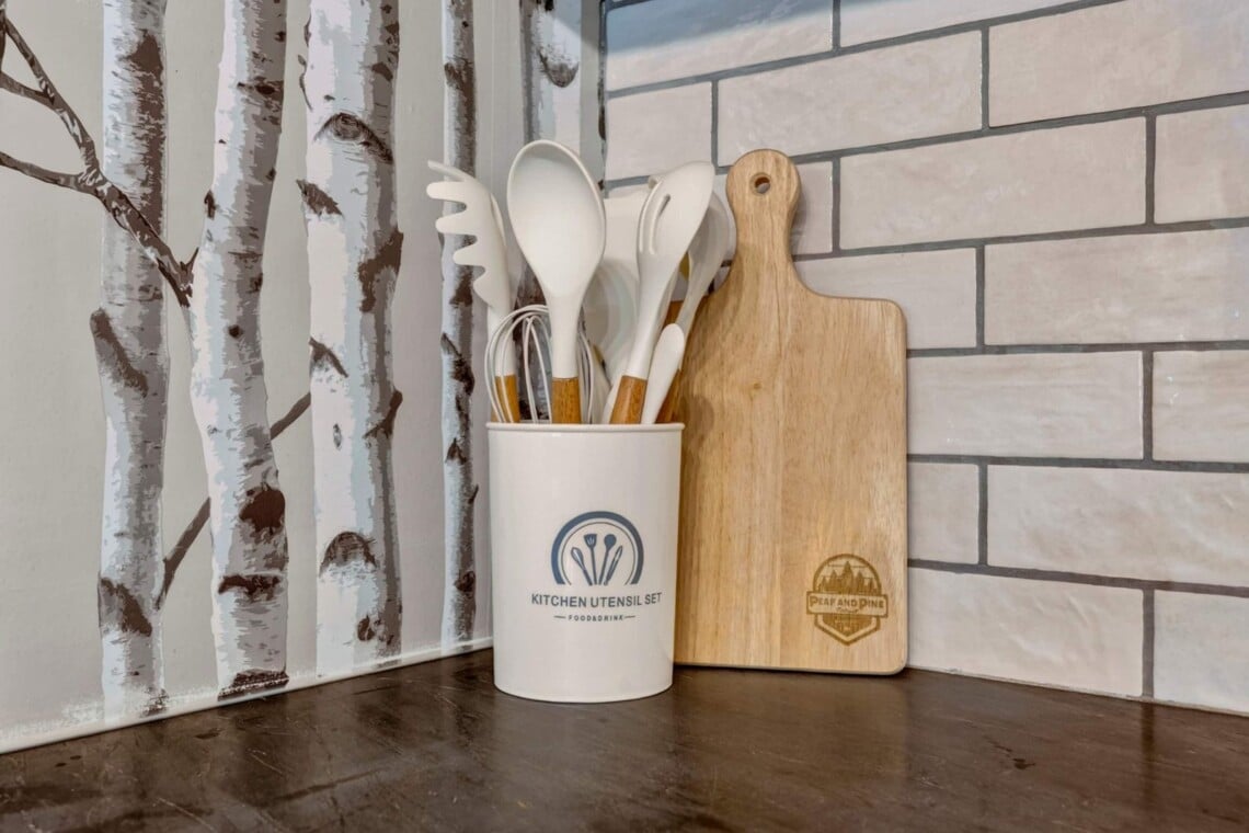 Utensil crock and wooden cutting board against birch tree wallpaper