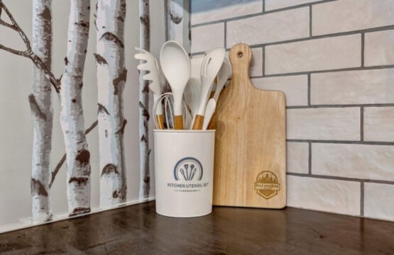 Utensil crock and wooden cutting board against birch tree wallpaper