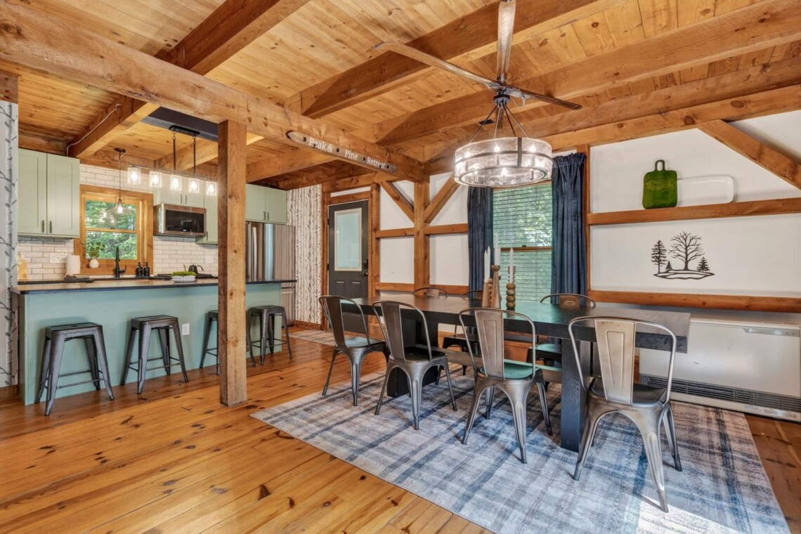 Dining table and kitchen island with bar stools under timber-frame beams