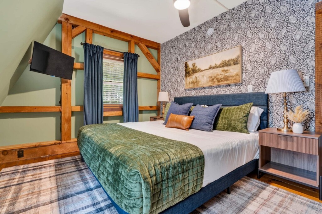 Bedroom with navy upholstered bed, green velvet quilt and wall-mounted TV