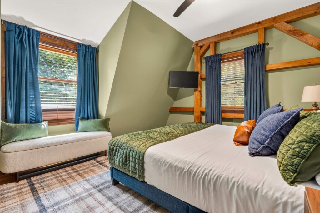 Bedroom with upholstered bench, blue curtains and timber-frame accents at Peak & Pine Retreat