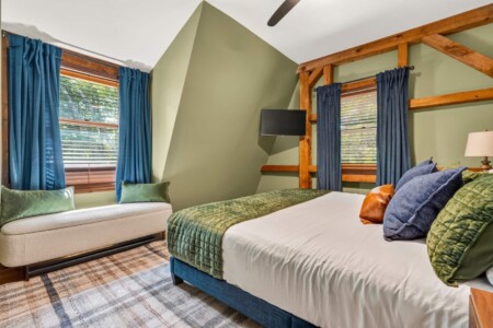 Bedroom with upholstered bench, blue curtains and timber-frame accents at Peak & Pine Retreat