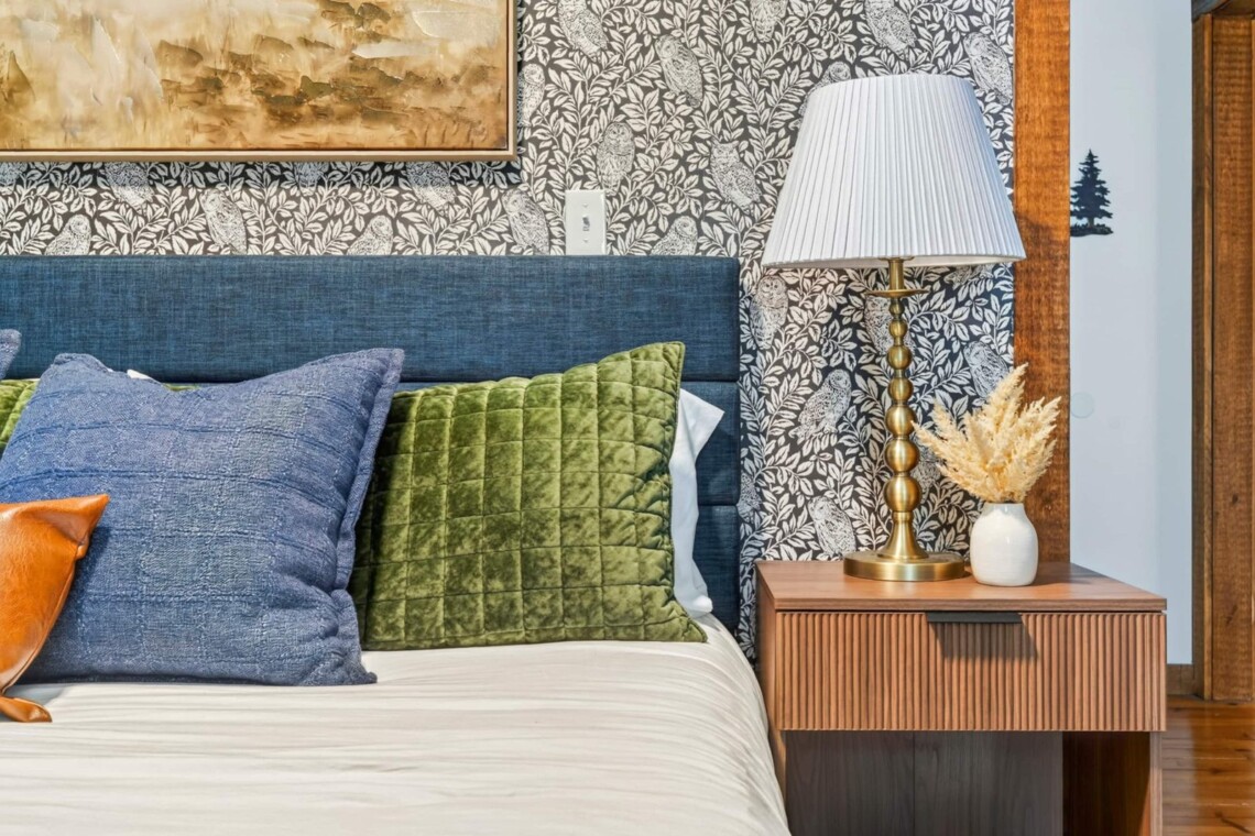 Bedside table with brass lamp beside a navy upholstered bed with velvet pillows
