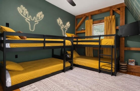 Two bunk beds with mustard bedding and neon antler art at Peak & Pine Retreat