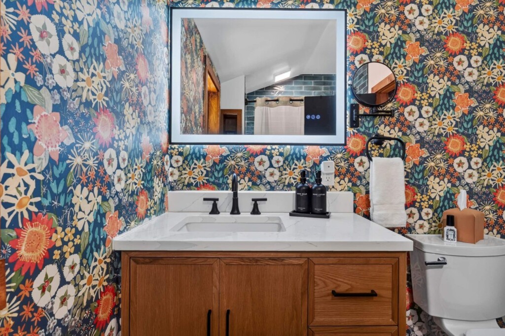 Bathroom with floral wallpaper, wood vanity and lighted mirror