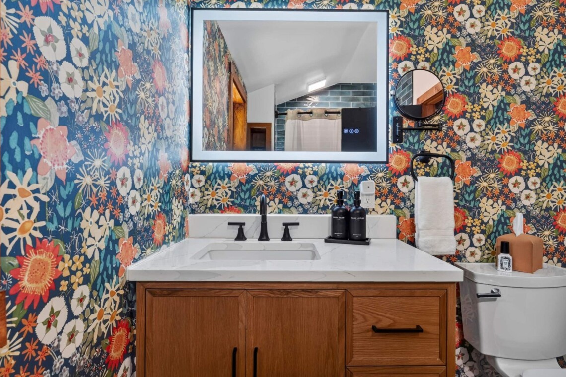 Bathroom with floral wallpaper, wood vanity and lighted mirror