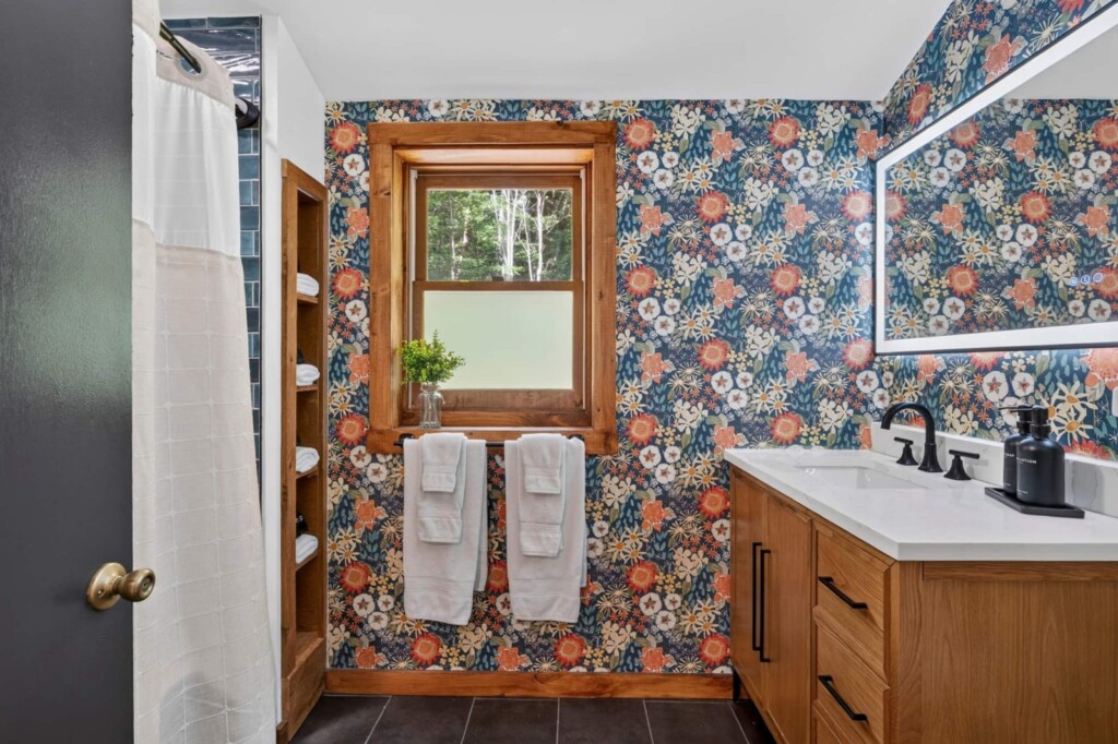 Floral wallpaper bathroom with shower curtain, window and wood vanity