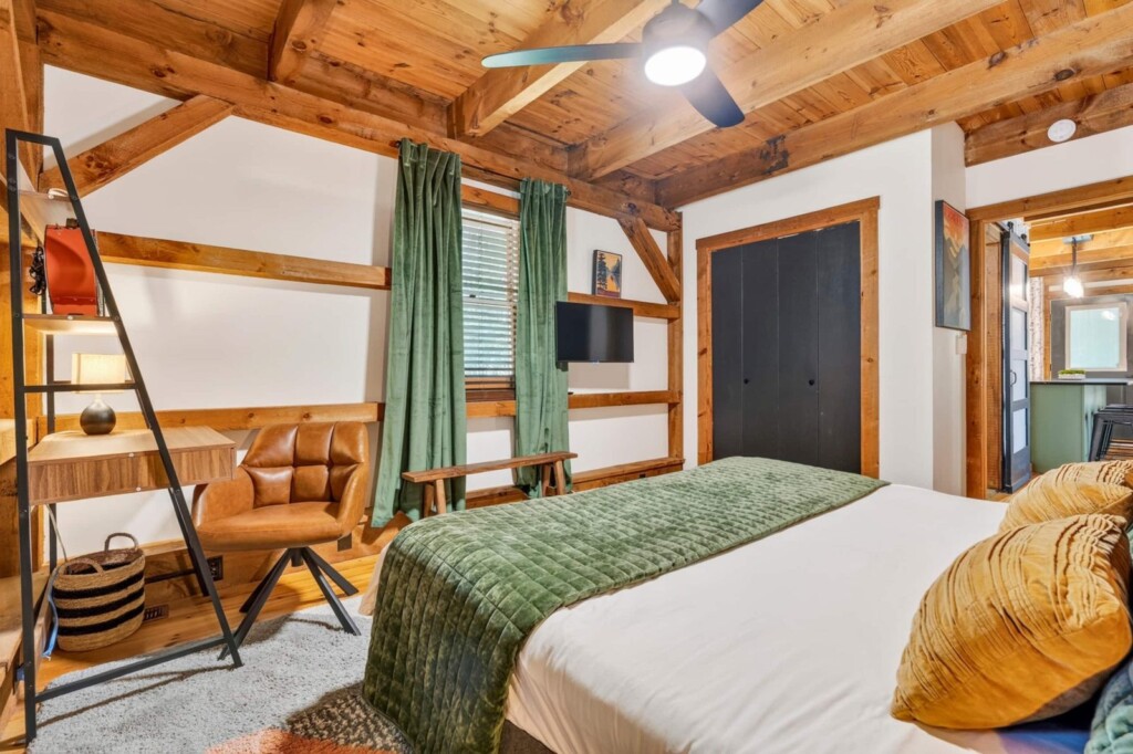 Bedroom with desk chair, green curtains and timber beams at Peak & Pine Retreat