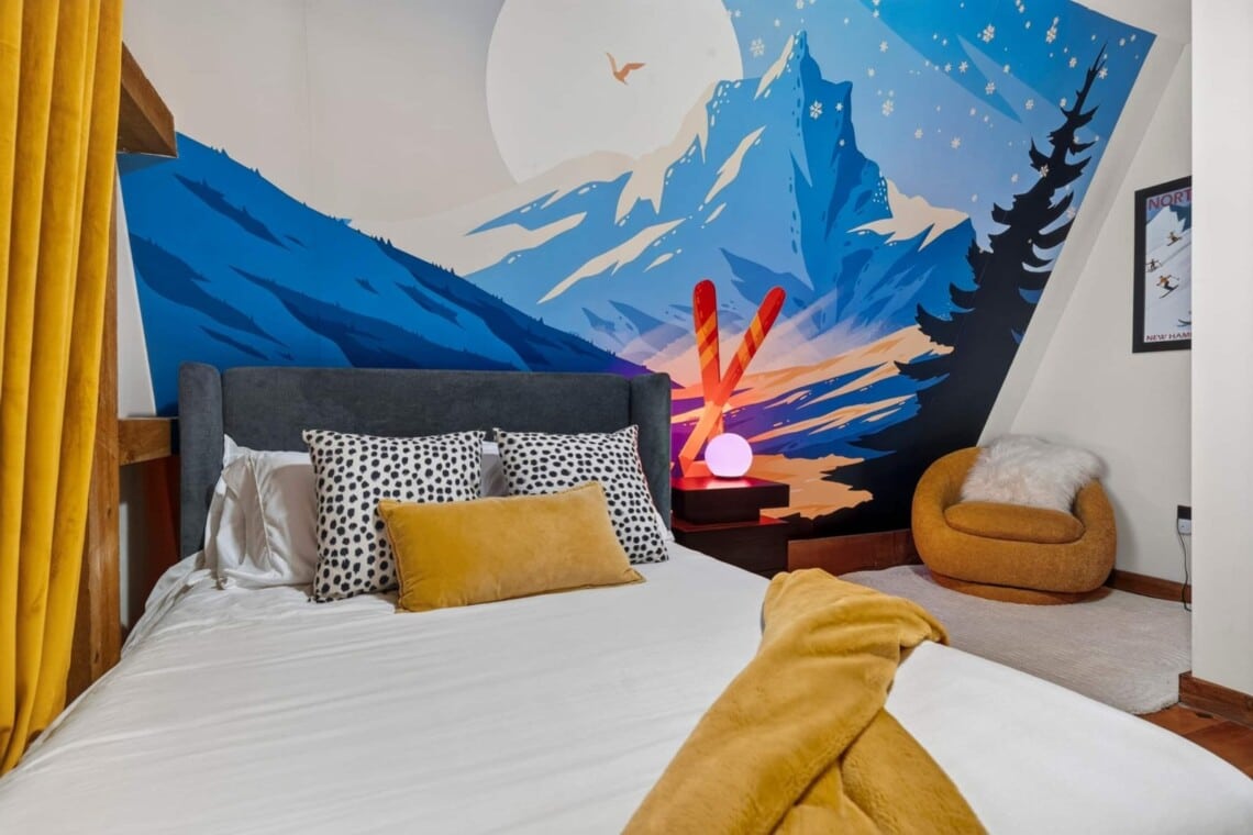Bed with patterned pillows under a vibrant painted mountain mural at Peak & Pine Retreat