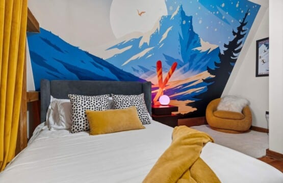 Bed with patterned pillows under a vibrant painted mountain mural at Peak & Pine Retreat