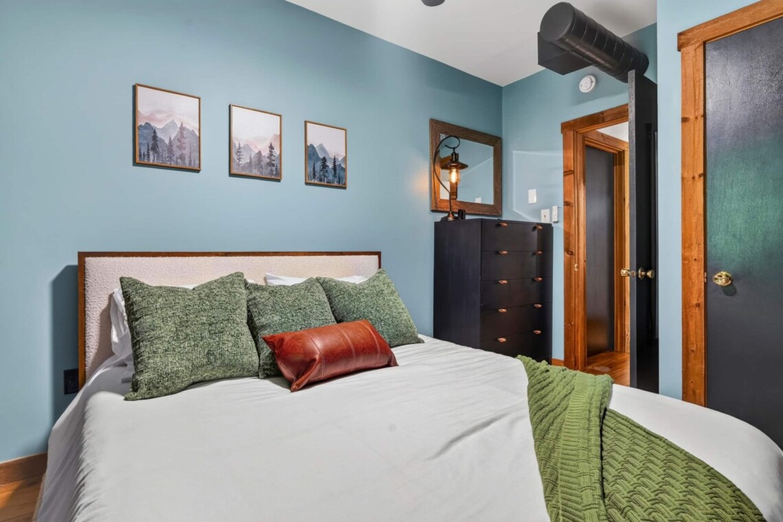 Blue bedroom with upholstered bed, green pillows and mountain art prints