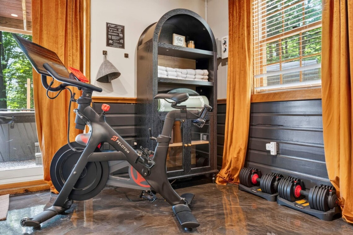 Peloton bike and dumbbell set in a corner with orange curtains