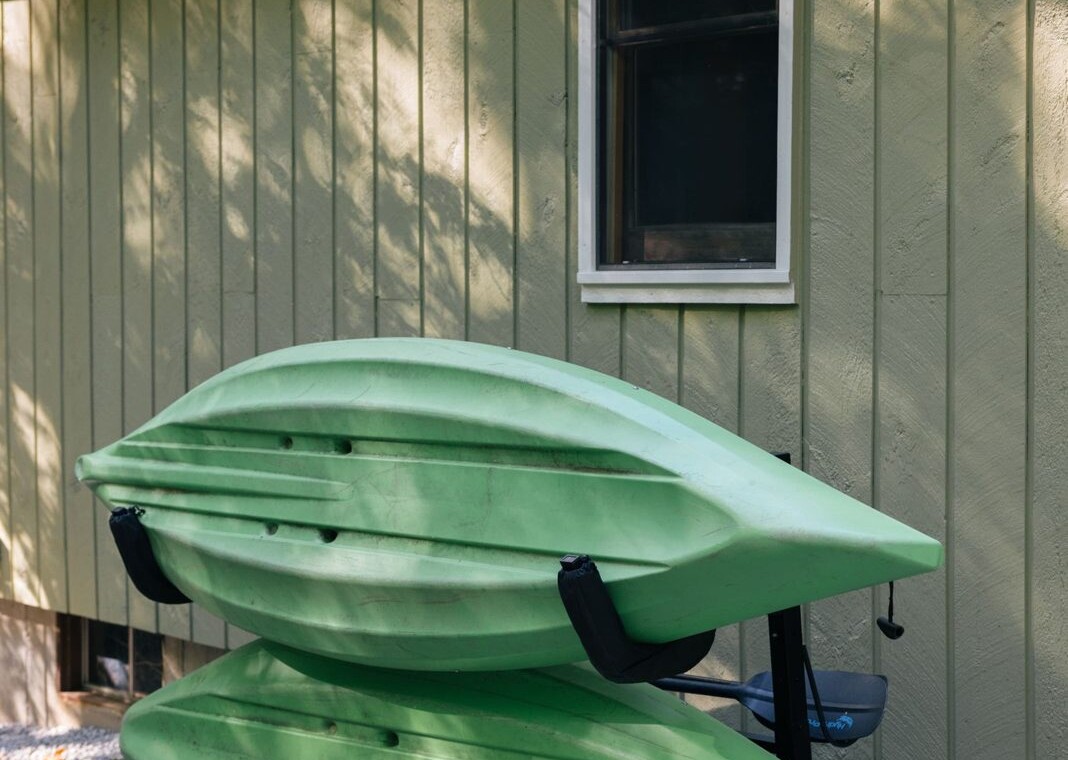 Two green kayaks on a rack beside the house